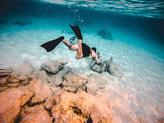 Woman snorkeling over underwater shipwreck ruins in clear blue ocean