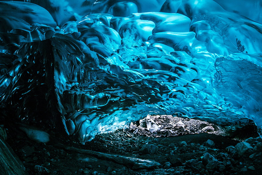 Glowing Blue Ice Cave Interior with Rocky Floor