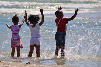 Three African Children Playing In Ocean Waves At Beach