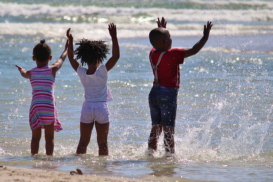 Three African Children Playing In Ocean Waves At Beach