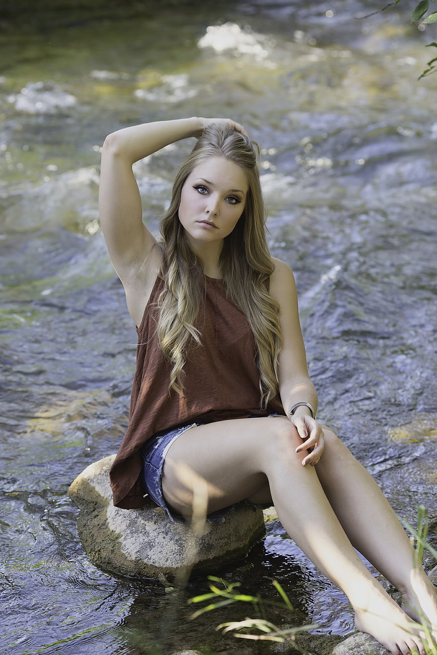 Young woman sitting on rock in flowing stream