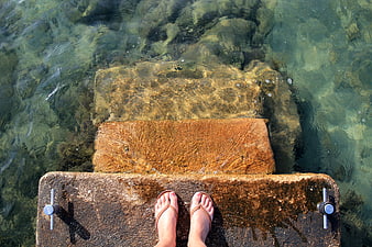 Feet in flip flops on stone steps in clear turquoise water