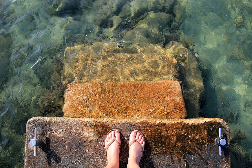 Feet in flip flops on stone steps in clear turquoise water
