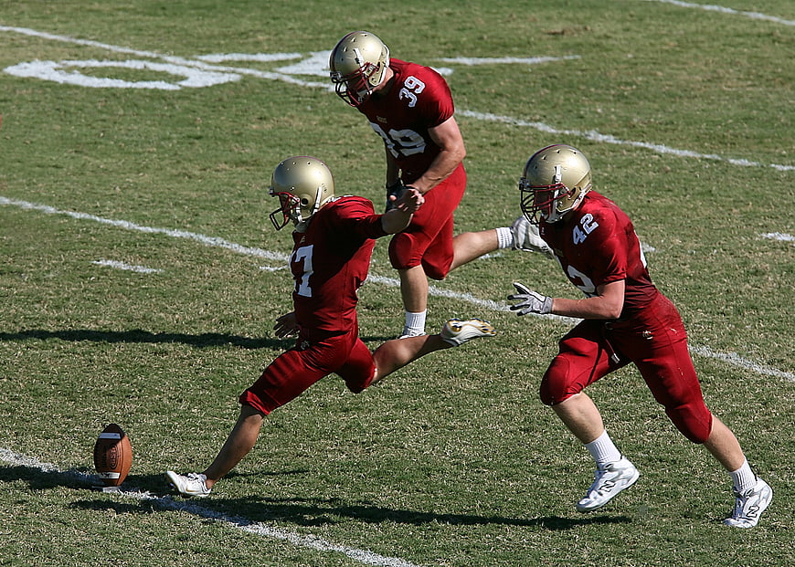 American Football Players Kicking Punt on Grass Field