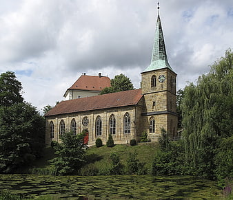 Historic stone church with spire by a lily pond