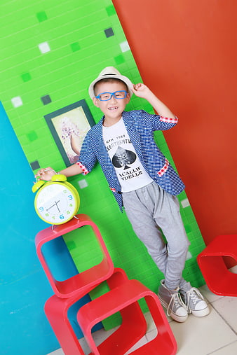 Stylish young boy posing with alarm clock in colorful studio