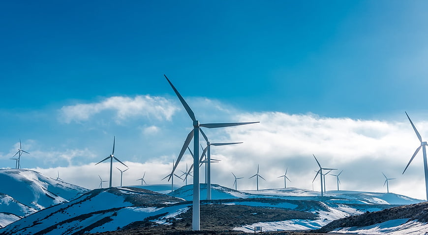 Wind Turbines On Snowy Hills Under Blue Sky