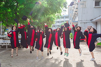 Happy Asian female graduates jumping with caps outdoors