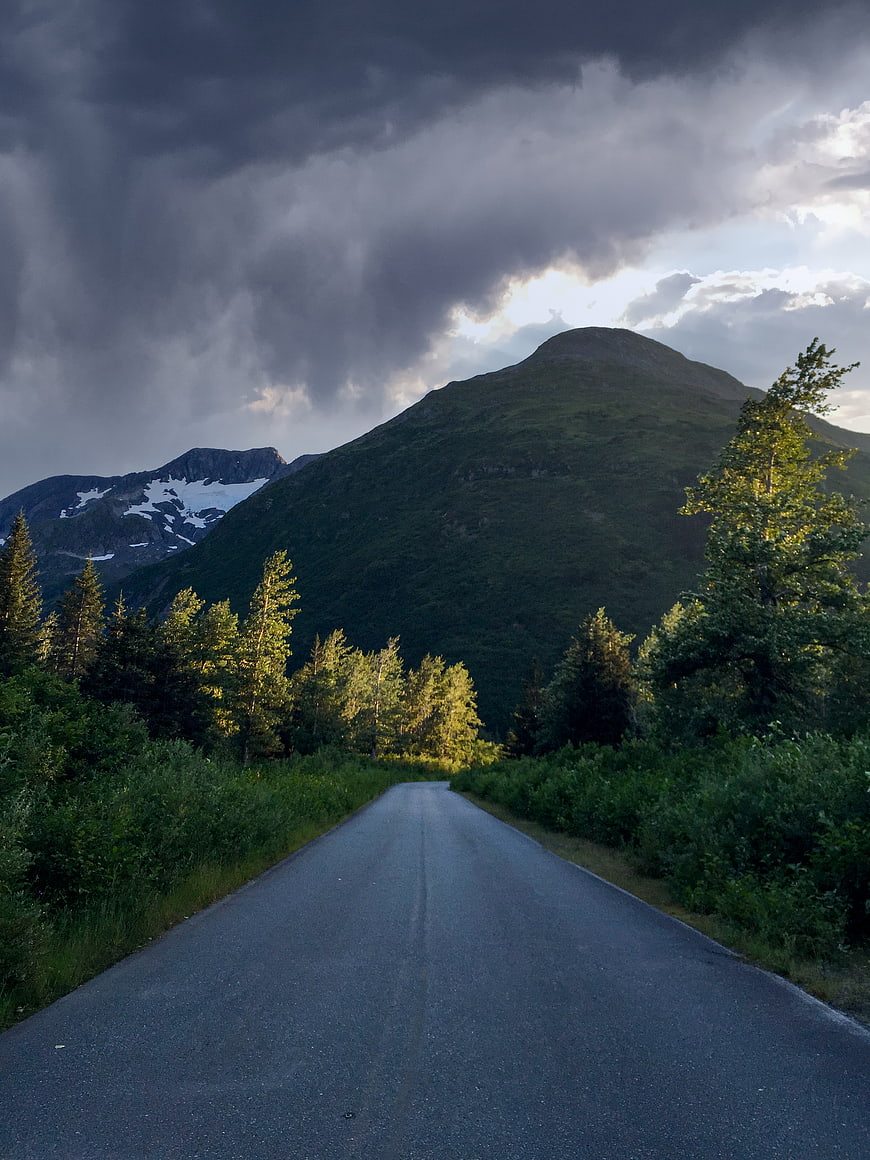 Dramatic Mountain Road with Stormy Sky and Sunlit Trees