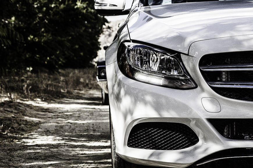 Close-up of white luxury car headlight on dirt road