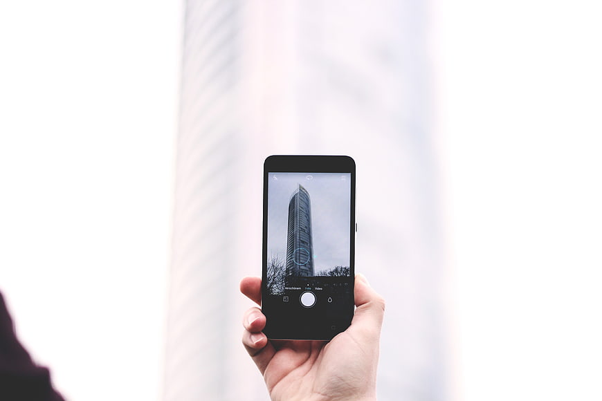 Hand holding smartphone taking photo of skyscraper