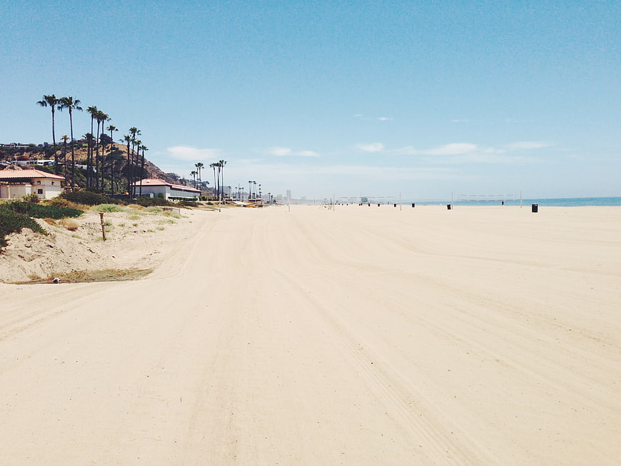 Wide sandy beach with palm trees and houses under blue sky