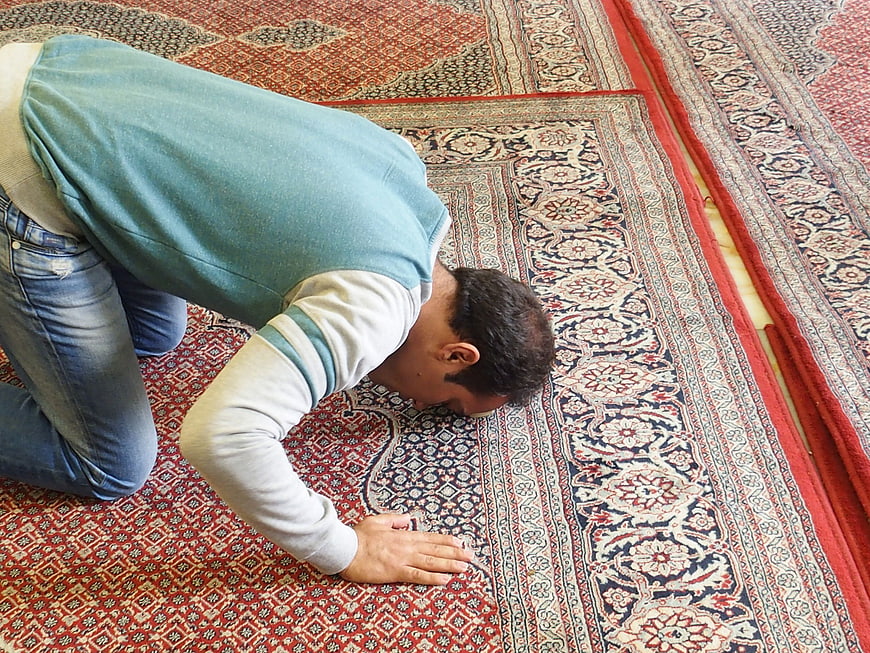 Muslim man praying on ornate Persian rug