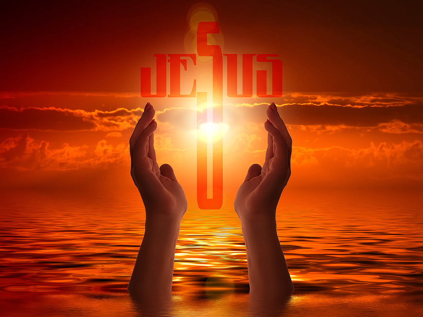 Praying Hands Holding Glowing Cross Against Orange Sunset Sky