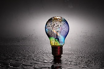 Rainbow light bulb with water droplets on wet dark surface