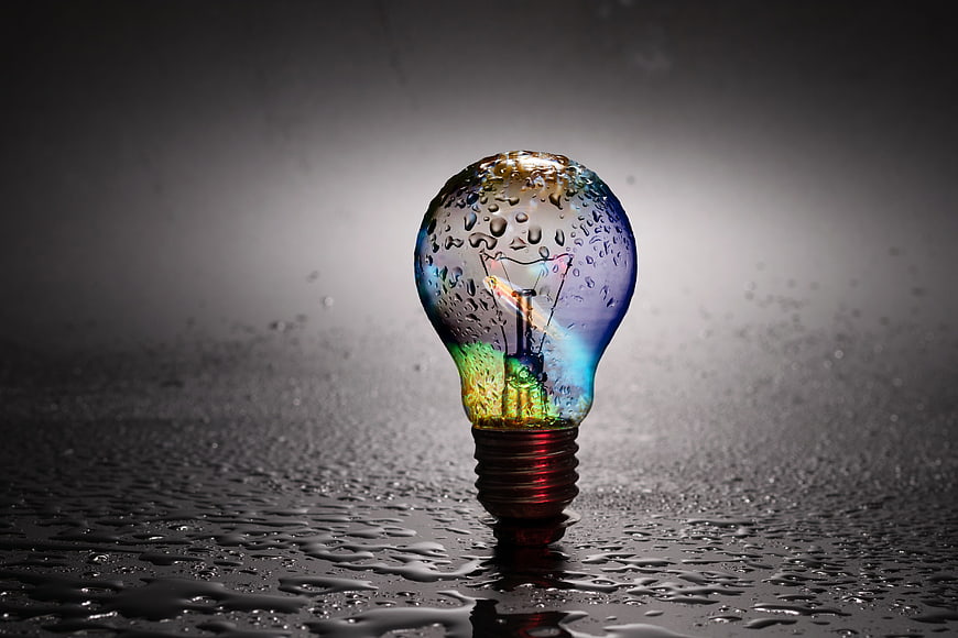 Rainbow light bulb with water droplets on wet dark surface