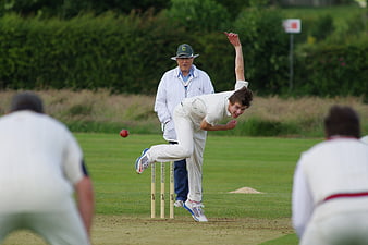 Cricketer bowling action shot on green pitch