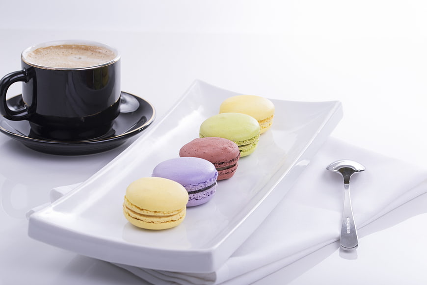 Colorful macarons and black coffee cup on white background