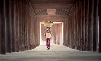 Woman carrying basket on head in wooden corridor