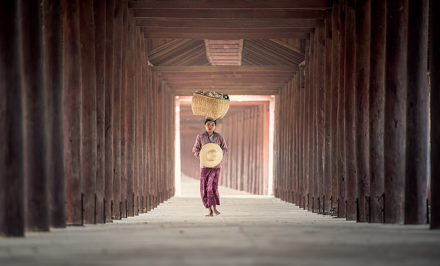Woman carrying basket on head in wooden corridor