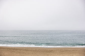 Foggy Beach Landscape with Calm Ocean Waves and Sand