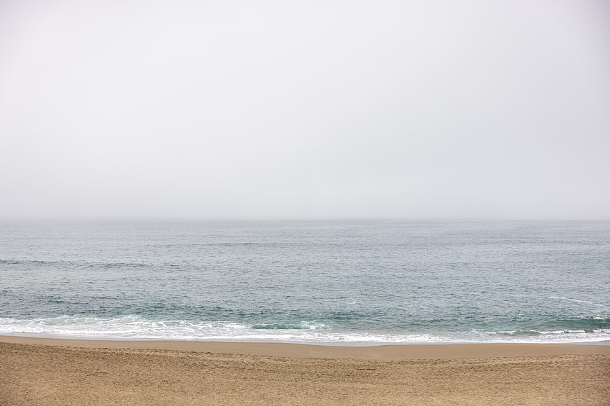 Foggy Beach Landscape with Calm Ocean Waves and Sand