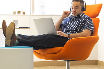 Man with Headphones Working on Laptop in Orange Chair