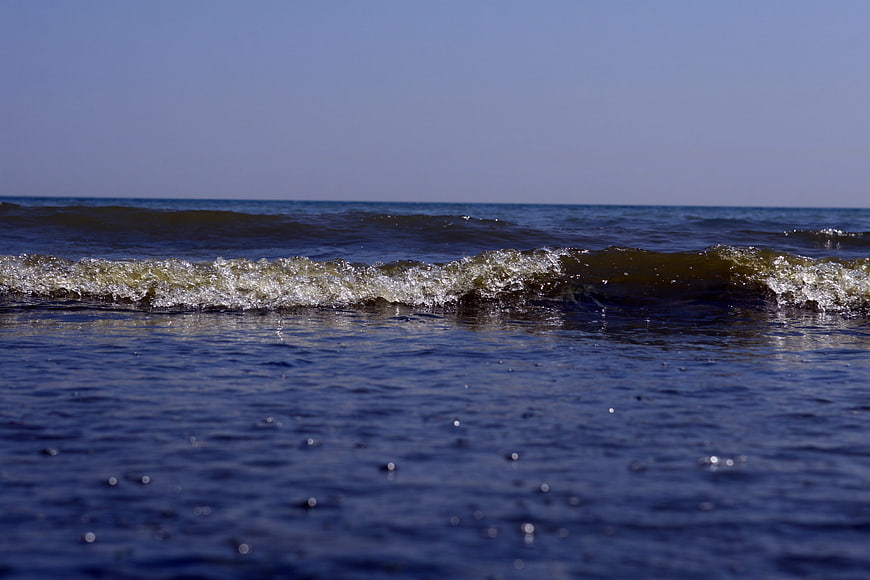 Low angle view of small ocean waves breaking on calm sea