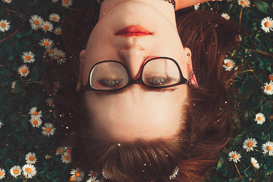 Upside down woman with glasses lying in daisies
