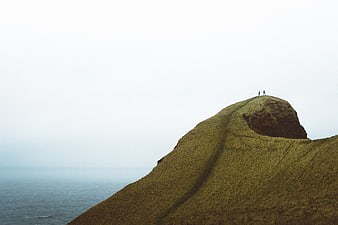 Two Hikers on Grassy Cliff Overlooking Ocean