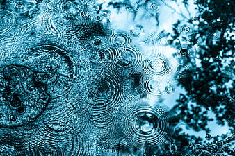 Blue raindrops on glass with ripples and blurred background
