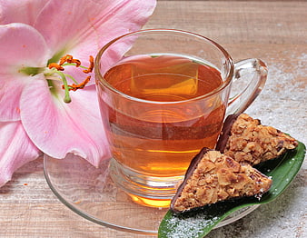 Glass cup of amber tea with nut cookies and pink lily blossom