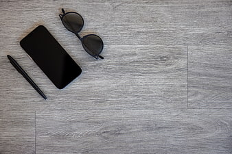 Minimalist flat lay of smartphone, sunglasses, and pen on gray wood