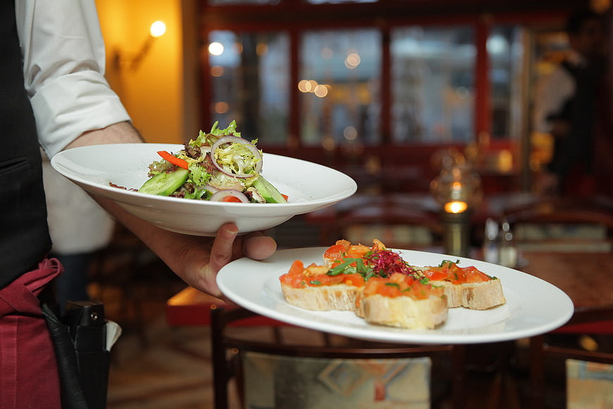 Waiter serving fresh salad and bruschetta in restaurant