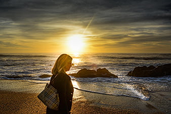 Woman with Plaid Bag Watching Golden Sunset on Rocky Beach