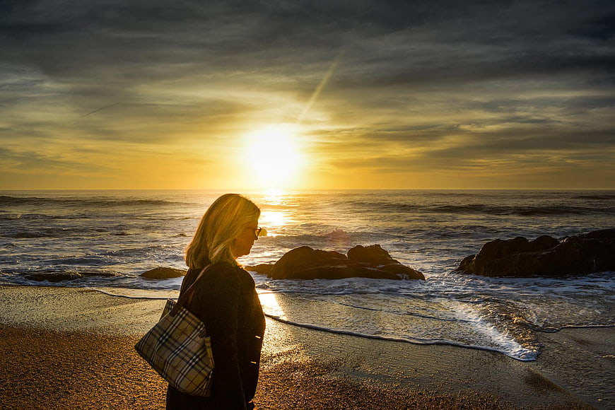 Woman with Plaid Bag Watching Golden Sunset on Rocky Beach