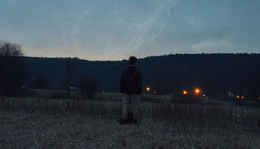 Young Man Standing in Field Under Starry Night Sky