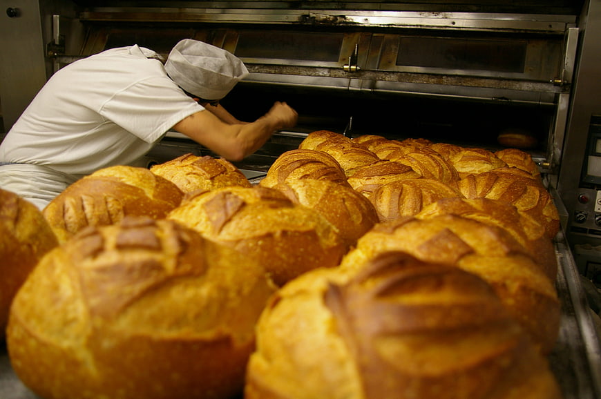 Baker Loading Fresh Golden Bread Loaves into Industrial Oven