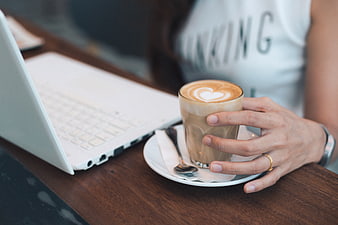 Woman holding latte with laptop on wooden table