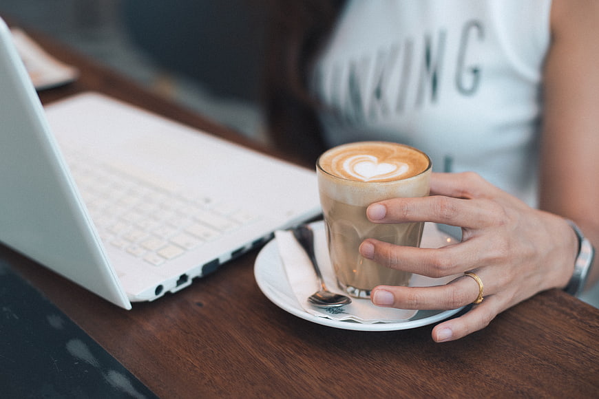 Woman holding latte with laptop on wooden table