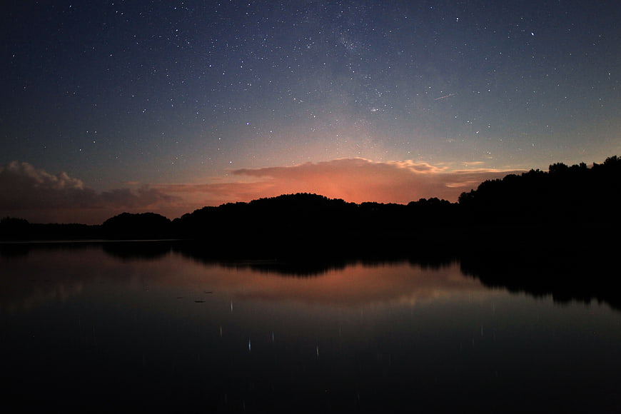 Starry Night Sky Over Lake with Silhouette Hills