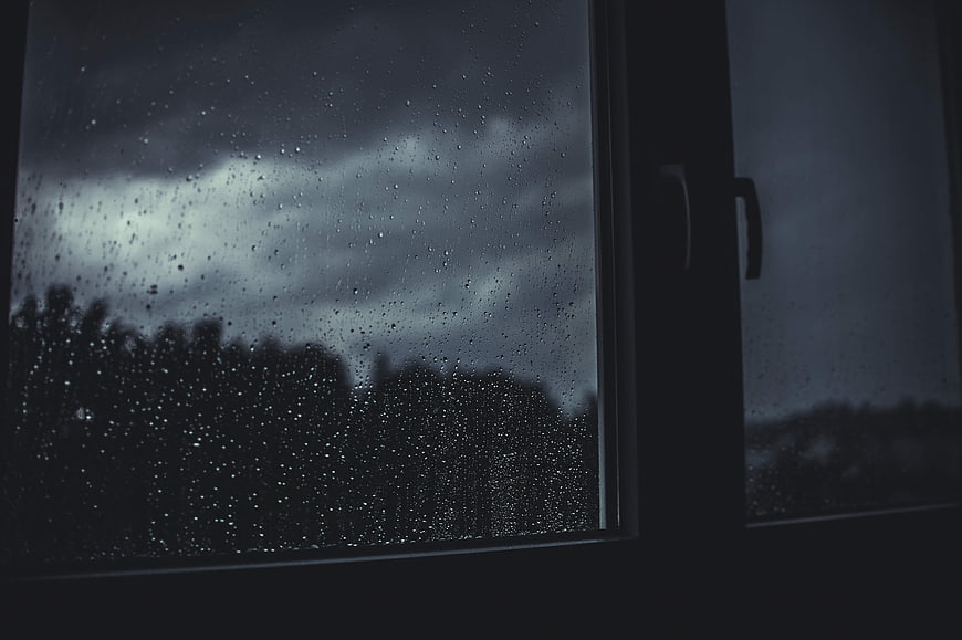 Raindrops on Window Glass Against Dark Stormy Sky