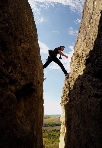 Man crossing a narrow gap between two tall rock cliffs