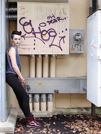 Edgy woman with blue hair leaning against urban graffiti wall