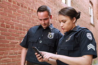Two police officers checking smartphone against brick wall