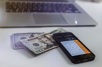Smartphone Calculator with US Cash and Laptop on Desk
