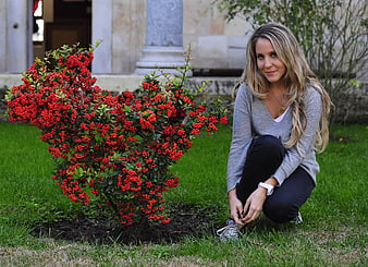 Young woman crouching beside red berry bush in garden