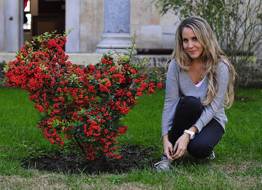 Young woman crouching beside red berry bush in garden
