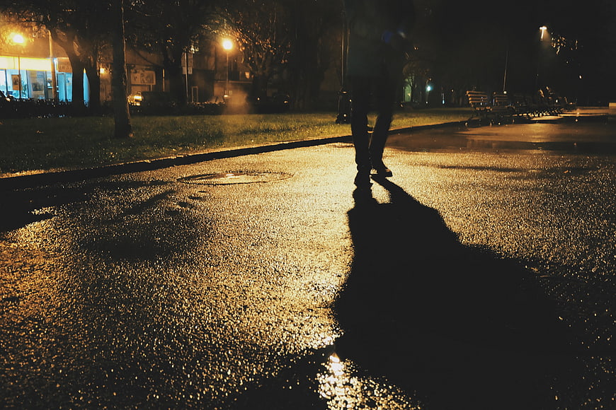 Silhouette of person walking on wet street at night