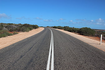 Empty asphalt road curving through arid landscape under blue sky